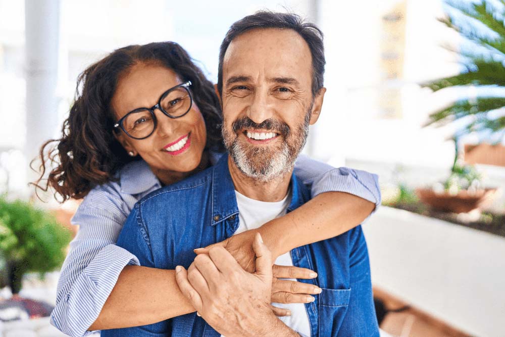Smiling couple embracing, showing confidence from healthy, beautiful smiles after Dental Implants