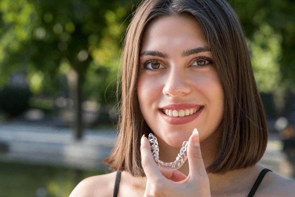 Woman holding clear aligner, showcasing Invisalign treatment in Jackson Hole, WY